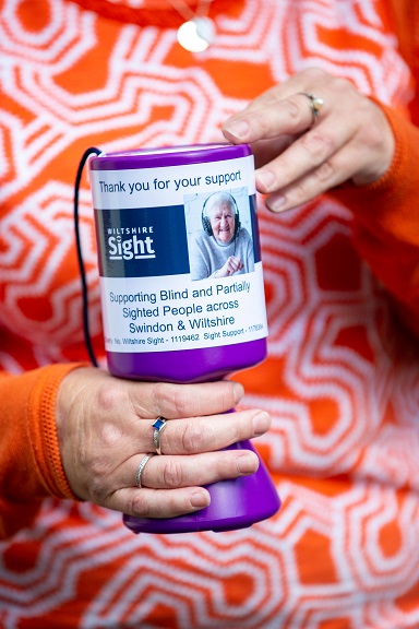 Image: A lady holding a collection box that says 'Thank you for your support'.