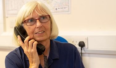 The picture shows a volunteer on the phone in reception in our resource centre.