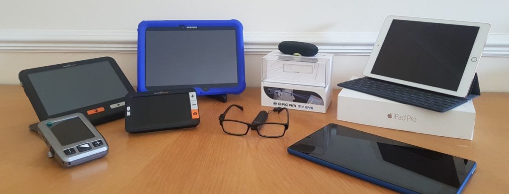 Photo of a variety of assistive technology, including iPad and ORCAM devices
