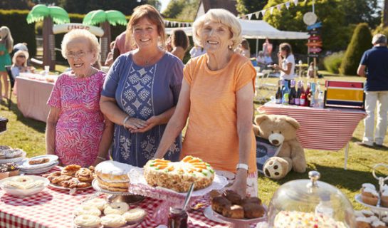 Portrait Of Women Serving On Cake Stall At Busy Summer Garden Fete