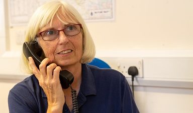 The picture shows a volunteer on the phone in reception in our resource centre.