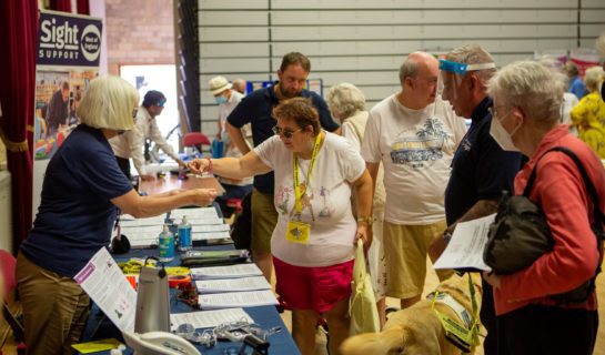 Phto shows event with guide dog users talking to Sight Support volunteer