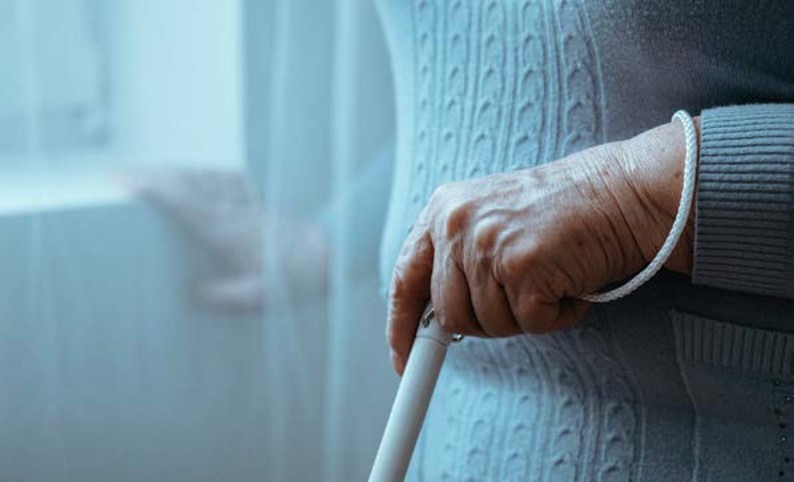 Person holding a cane standing next to a door.