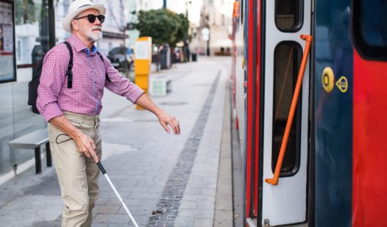 A man is using a cane and about to get on a bus.