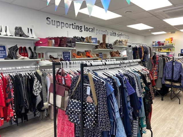 Inside view of Wiltshire Sight charity shop, view is of rails of clothing and numerous shelves on the back wall holding shoes and bags