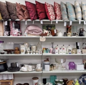 5 shelves of items for sale, assorted kitchenware and colourful cushions