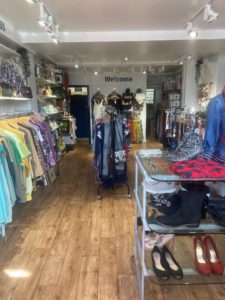 The inside of our shop, clothes are on racks at the side and there is a feature table in the middle of the wooden floor.