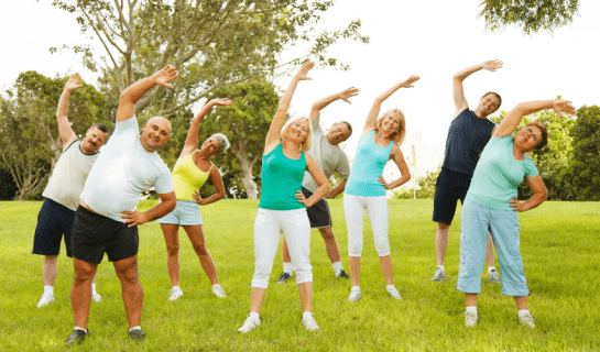 8 people are standing outside exercising together, they all have their right arm over their head and are leaning to the left stretching.