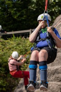 Image of two people one person is abseiling and ins hanging while wearing climbing gear.