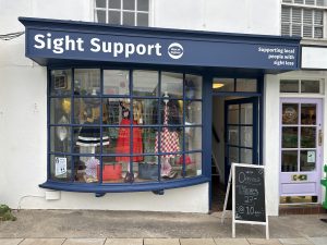 Our Thornbury charity shop has a dark blue bay window with a colourful display of clothing. Our logo is at the top of the window.