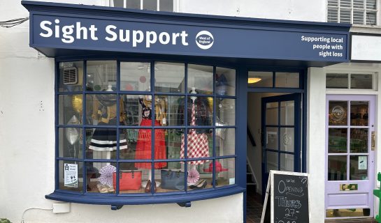 Our Thornbury charity shop has a dark blue bay window with a colourful display of clothing. Our logo is at the top of the window.