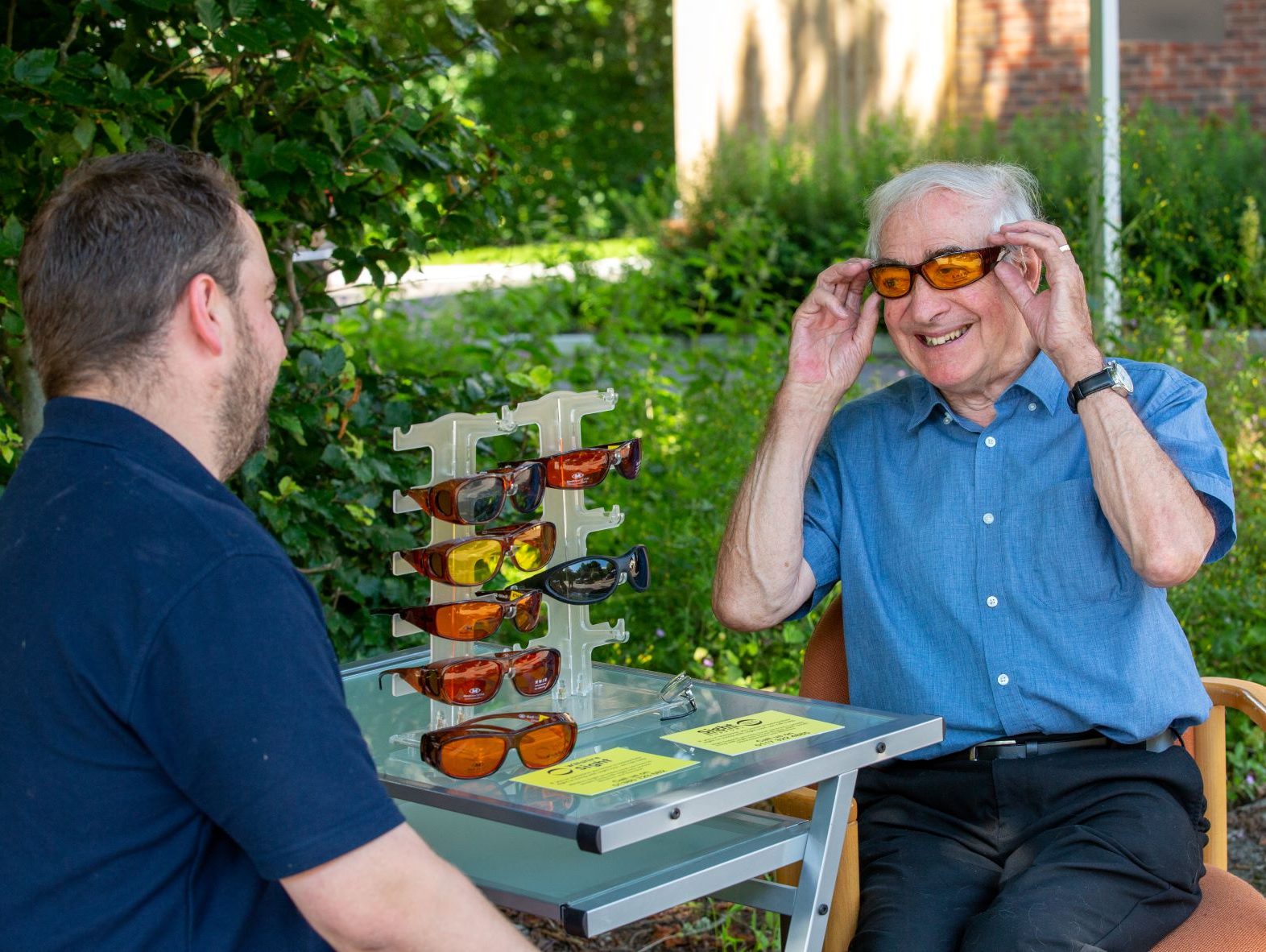 A Community Sight Loss Advisor is sitting outside with a gentleman who is trying out some eyeshields.