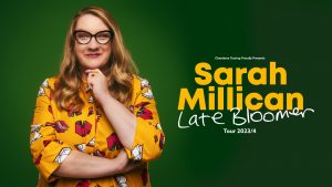 Sarah Millican is facing the camera and smiling, she is wearing black rimmed glasses and an orange top. Behind her is a green background. Text reads Chambers Touring proudly presents Sarah Millican Late Bloomer Tour 2023/2024