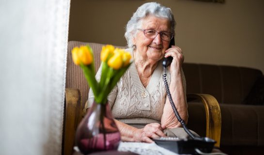 An elderly lady is sat at a table having a chat to someone on the telephone