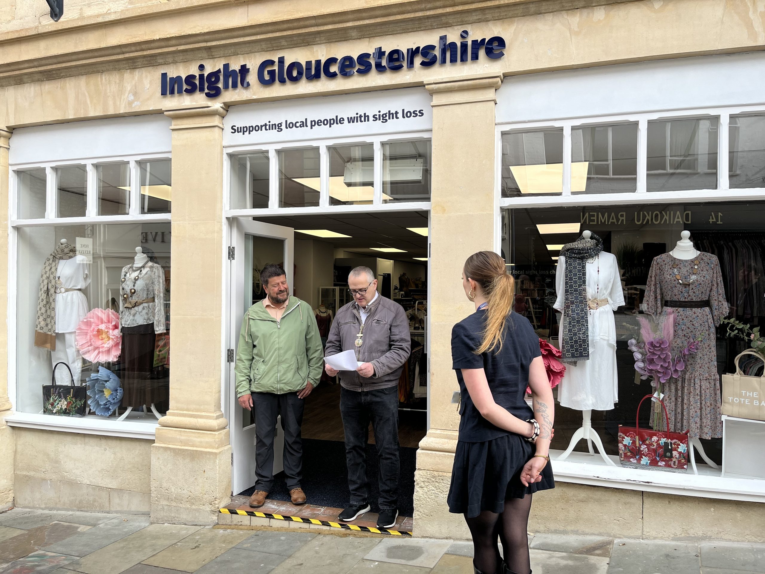 The Mayor of Stroud stands outside the new Insight Gloucestershire charity shop holding notes as he gives a speech. Next to him is the Chair of Trustees