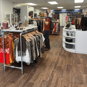 Inside the new Insight Gloucestershire charity shop in Stroud. Racks of clothes, shoes and accessories are on display, with wide walkways and a bright, open layout. A man carrying a toddler is chatting to another person near the centre of the shop.