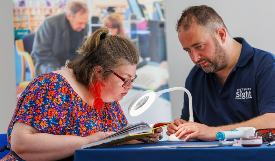 A sight loss advisor and lady are sitting at a table exploring equipment.
