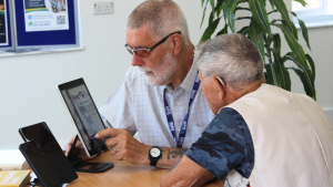 A digital skills Tech Buster volunteer looking at accessibility features on a tablet with an older man.